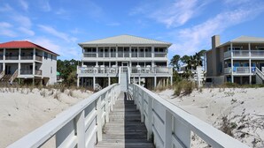 Une propriété située en bord de mer, avec une promenade en bois menant à un grand bâtiment doté de nombreux balcons.