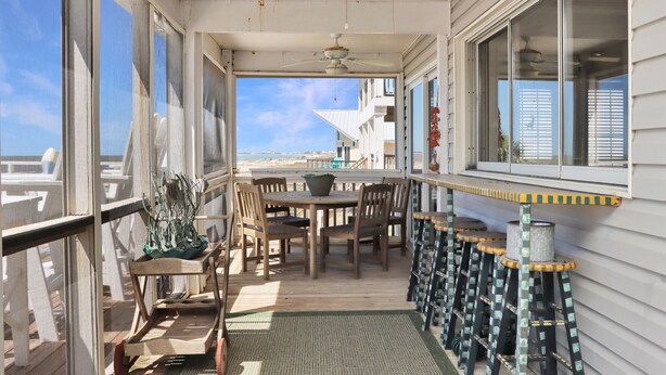 Un espace extérieur abrité, doté d’une table et de chaises, d’un ventilateur de plafond et offrant une vue sur la plage.
