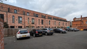 Een parkeerplaats met verschillende auto's geparkeerd voor een gebouw van baksteen met meerdere ramen en balkons.