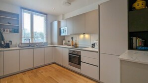 Een moderne keuken met witte kasten, een ingebouwde oven en een raam met zonwering.