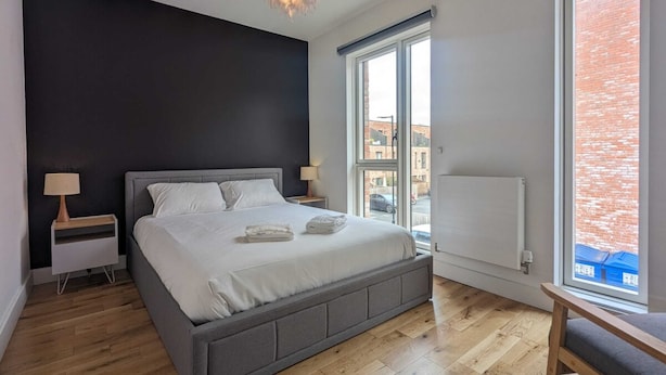 Een moderne slaapkamer met een groot bed, een raam met uitzicht op een bakstenen gebouw en een radiator aan de muur.