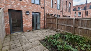 Een gebouw van baksteen met een houten hek, een bestraat terras en een tuin.