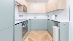 A compact kitchen with light blue cabinets, a white countertop, and a herringbone wood floor. - Luxuriously Compact 1BD Eco Home Clapham Common! (London)