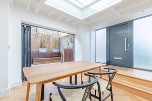 A modern dining area with a wooden table and chairs, a sliding glass door leading to an outdoor space, and a dark-colored door. - Luxuriously Compact 1BD Eco Home Clapham Common! (London)