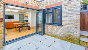 A modern patio with a glass door leading to a living area, a wooden table, and a sofa. - Luxuriously Compact 1BD Eco Home Clapham Common! (London)