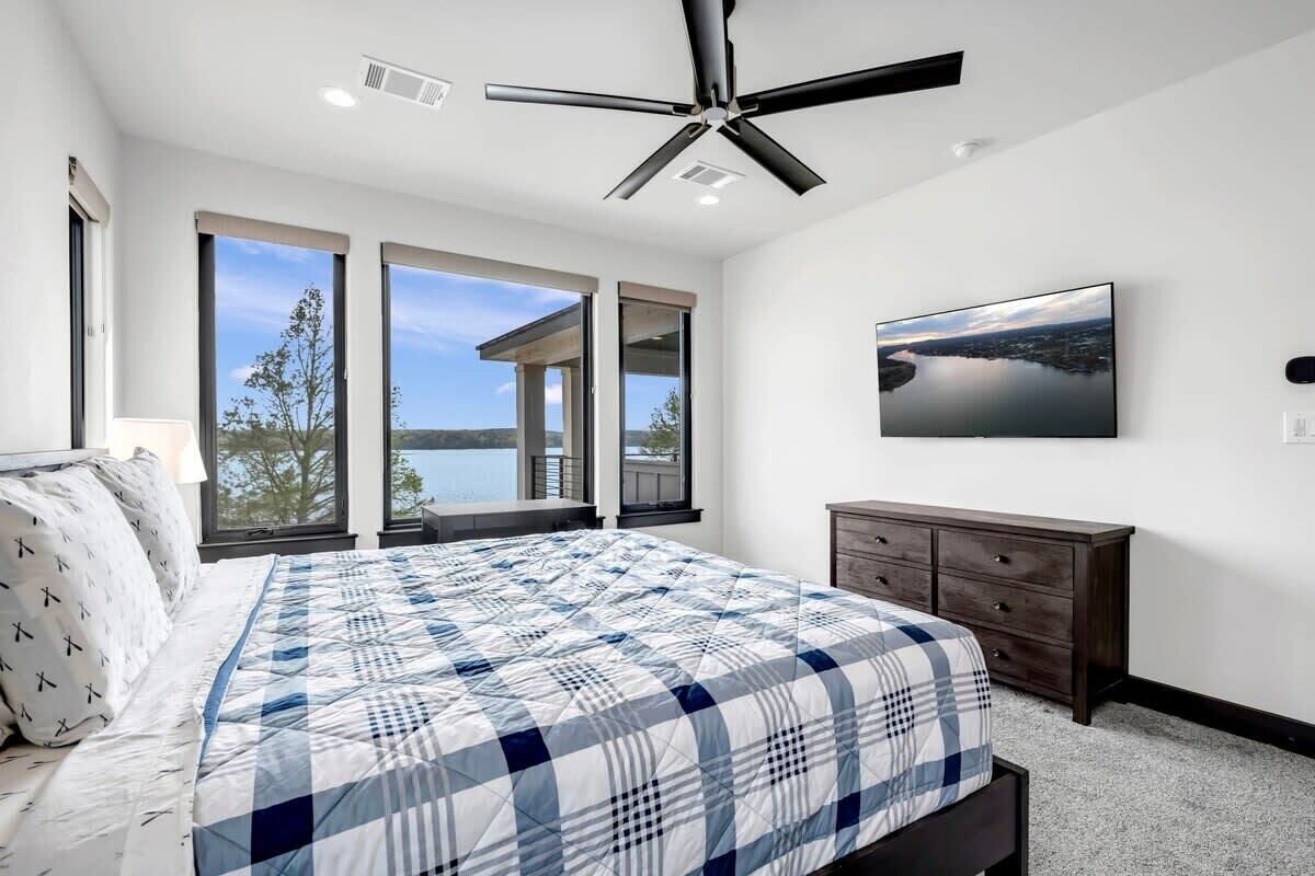 A bedroom with a large bed, a ceiling fan, a view of the outdoors, a dresser, and a painting on the wall.