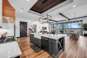 A modern kitchen with a large island, dark cabinetry, and a view to the outdoors.