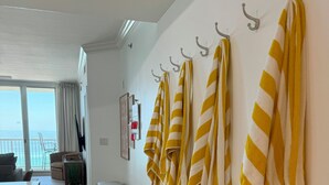 A hotel room with a balcony, a trash bin, a wicker basket, and towels hanging on hooks. - Azure #613 Updated Top Floor 3bdrm Sleeps 10! Views Galore! (Fort Walton Beach)