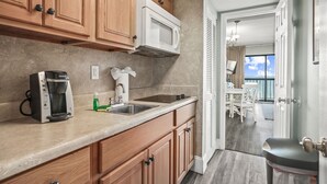 A compact kitchen with wooden cabinets, a built-in microwave, a coffee maker, and a sink. - Vacations By The Sea at Ocean Dunes Tower 1 (Myrtle Beach)