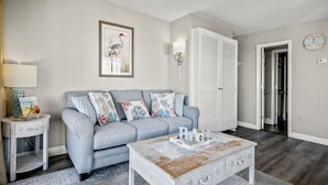 A living room with a grey sofa, a coffee table, a side table, a framed picture, a lamp, and a closet. - Vacations By The Sea at Ocean Dunes Tower 1 (Myrtle Beach)