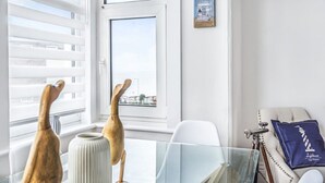 A modern room with a large window, a view of a cityscape, a white chair, a glass table, and a decorative item on the wall. - Sea Breeze-Cliff Terrace -Hunstanton. 3 Bedroom Apartment -Sea View  (Hunstanton)
