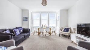 A modern living room with a sofa, dining table, chairs, and a television. - Sea Breeze-Cliff Terrace -Hunstanton. 3 Bedroom Apartment -Sea View  (Hunstanton)