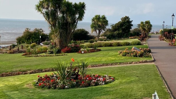 A landscaped garden with a pathway, palm trees, and a view of the ocean. - Sea Breeze-Cliff Terrace -Hunstanton. 3 Bedroom Apartment -Sea View  (Hunstanton)