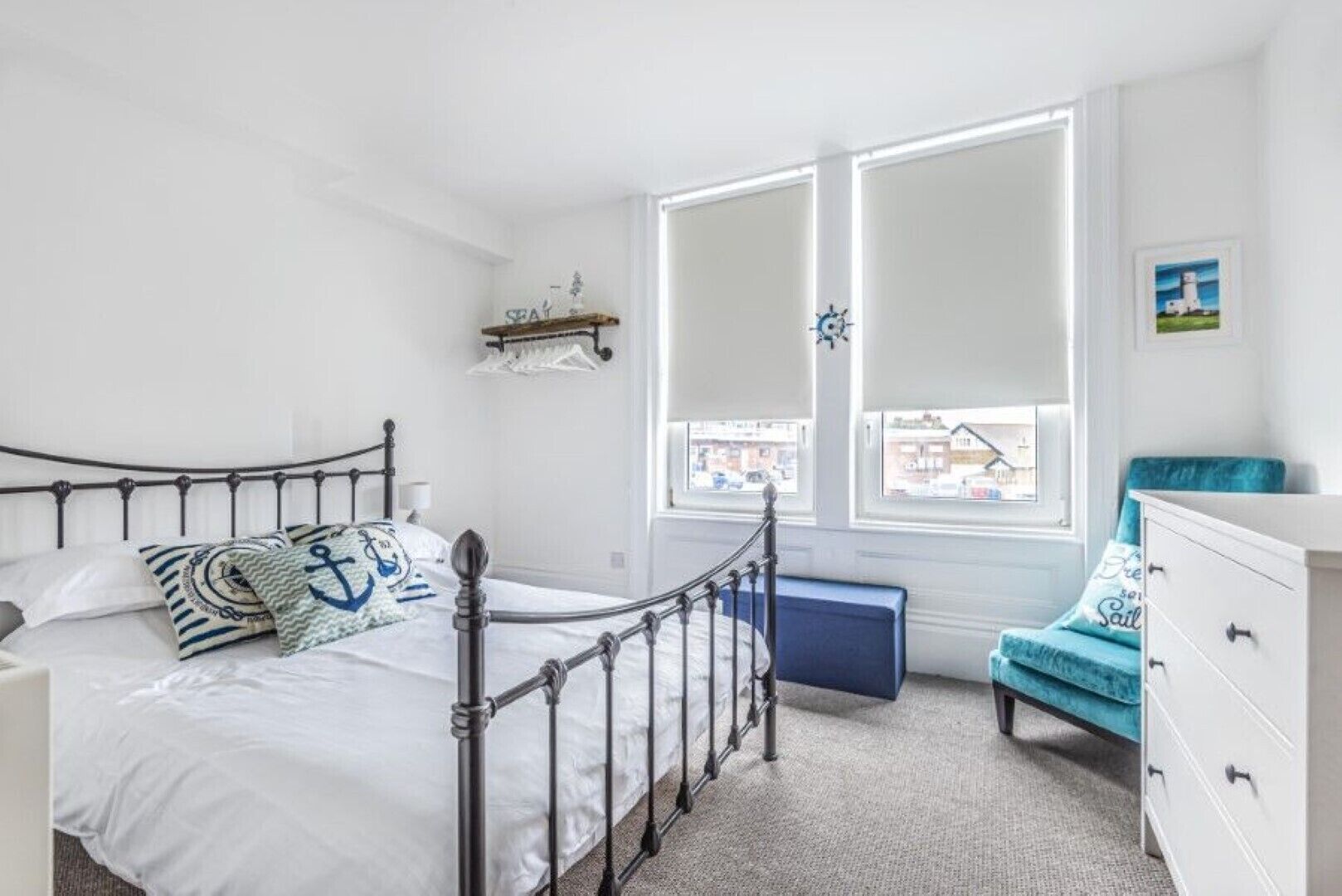 A bedroom with a metal bed frame, a white dresser, a blue chair, and a window with a view of buildings.