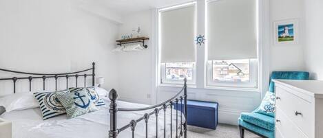 A bedroom with a metal bed frame, a white dresser, a blue chair, and a window with a view of buildings.