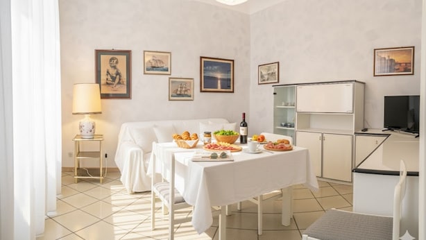 Una habitación bien iluminada con una mesa lista para el desayuno, una cama, un televisor y un mueble pequeño.