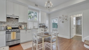 Une cuisine moderne avec des meubles blancs, une cuisinière en acier inoxydable et une table à manger en bois, assortie de chaises blanches.