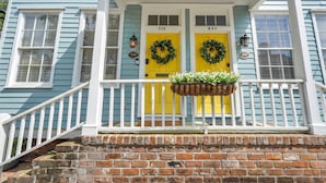 Une maison à deux étages avec un porche, des portes jaunes et des fondations en briques.