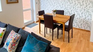 A dining area with a wooden table and chairs, a black sofa with colorful cushions, and a patterned wallpaper. - Spacious 3 Bed Townhouse Garden Wifi Balham (London)