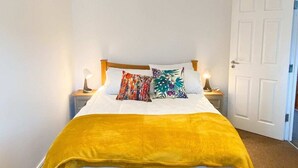 A bed with a yellow blanket, a floral pillow, and a bedside table with a lamp. - Spacious 3 Bed Townhouse Garden Wifi Balham (London)
