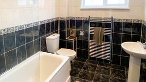 A bathroom with a bathtub, toilet, and sink, featuring black and white tiles and a window. - Spacious 3 Bed Townhouse Garden Wifi Balham (London)