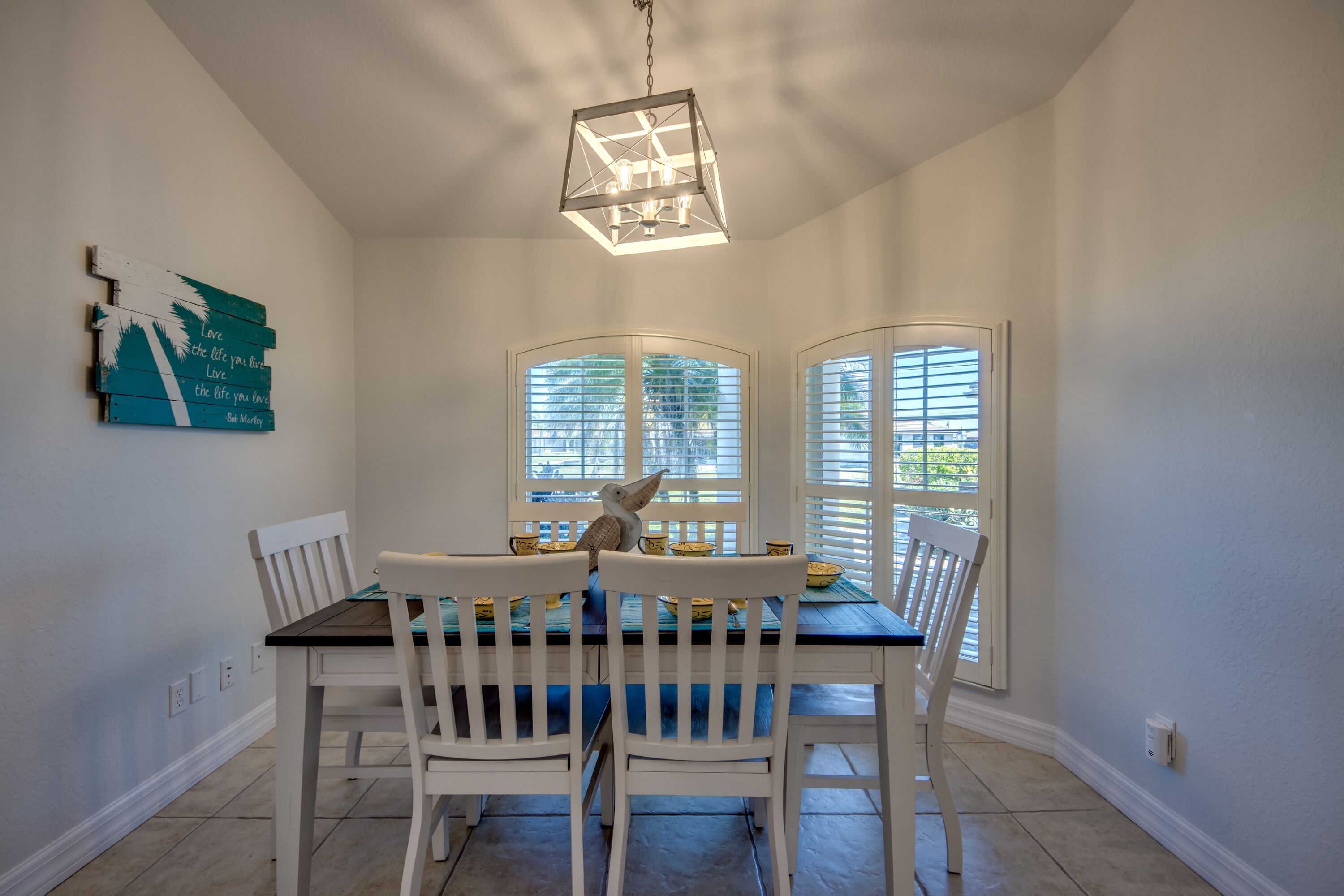 A dining area with a table, chairs, a chandelier, and a wall decoration.