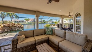 A covered outdoor seating area with a pool view, wicker furniture, and ceiling fans.