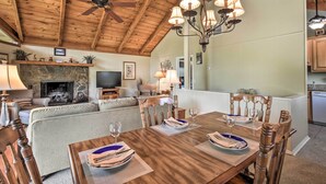 Un salon chaleureux avec une cheminée, un plafond en bois et un coin repas avec une table mise pour quatre personnes.
