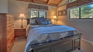 Une chambre à coucher avec un lit en bois, deux lampes de chevet, une commode et une fenêtre donnant sur des arbres.