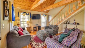 A cozy living room with a wooden ceiling, a sofa, a patterned armchair, and a staircase with wooden steps. - Nautical Retreat at Kudzu Cove Cabins Resort (Guntersville)