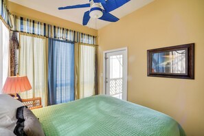 A room with a bed, a ceiling fan, a door, and curtains.