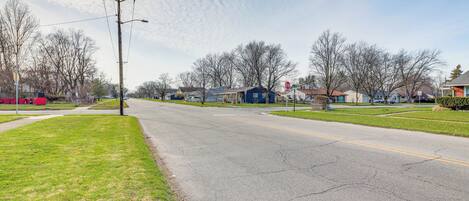 A suburban street with houses, a stop sign, and a grassy area.