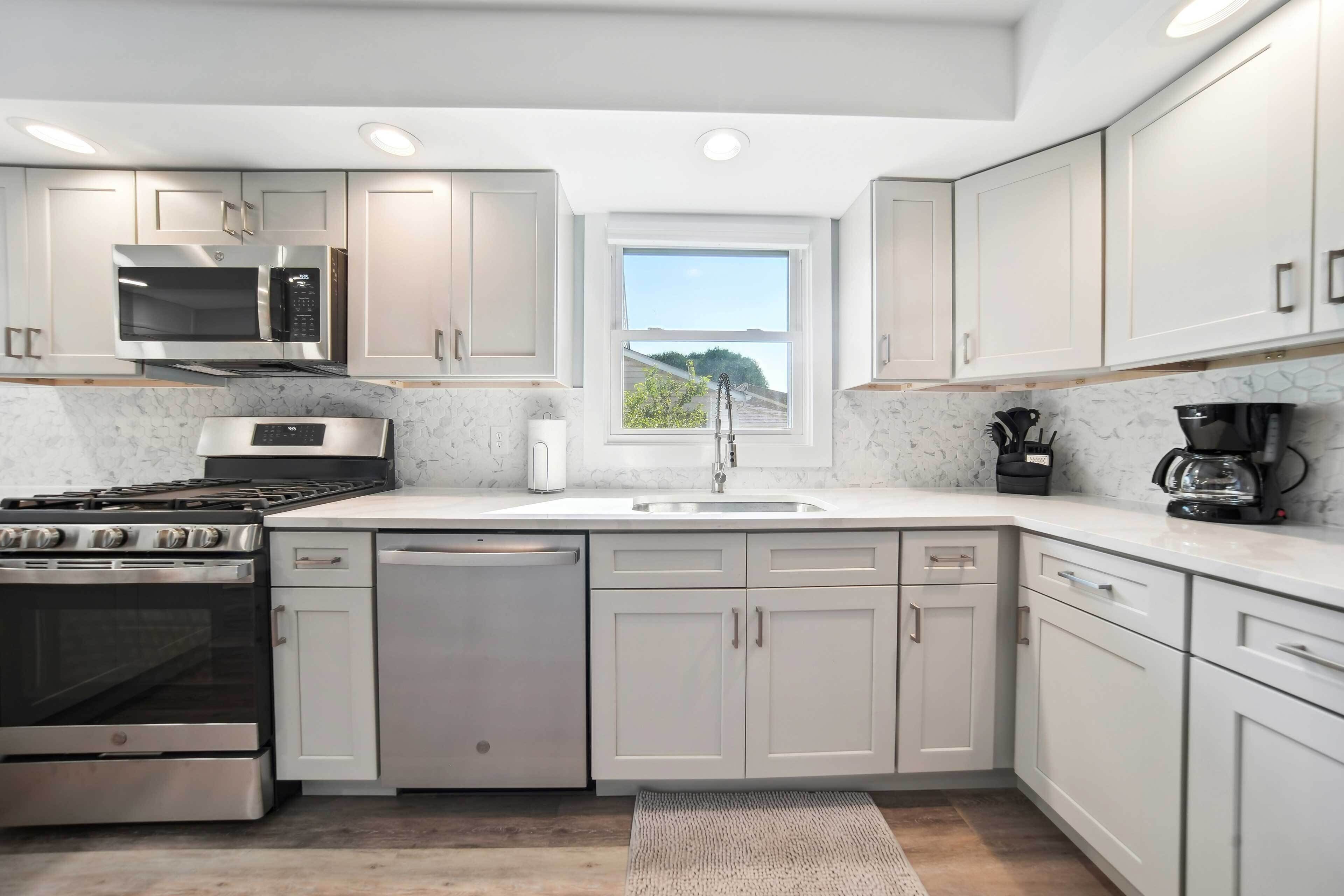 A modern kitchen with stainless steel appliances, white cabinetry, and a window providing natural light.