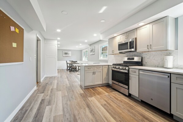 A modern kitchen with white cabinets, stainless steel appliances, and a herringbone wood floor.