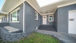 Ein modernes Haus mit grauem Backstein-Fassade, einer weißen Garagentür und einem kleinen Vorgarten mit Kiesweg und Rasenfläche.