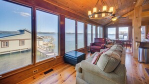 Ein geräumiges Zimmer mit großen Fenstern, das Blick auf einen Steg und Wasser bietet, mit Holzboden, einer Couch und einem Deckenventilator.