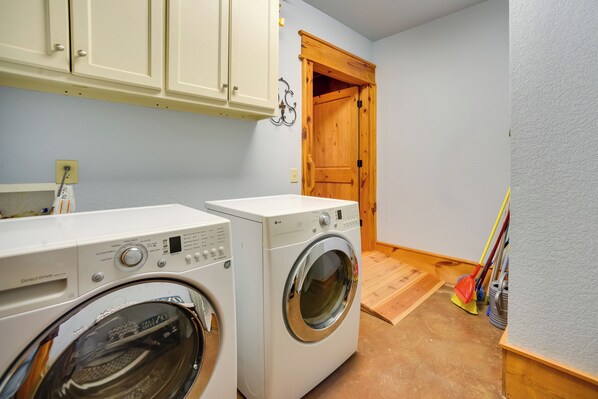 A laundry room with two white washing machines, wooden cabinets, a wooden door, and a broom leaning against the wall.
