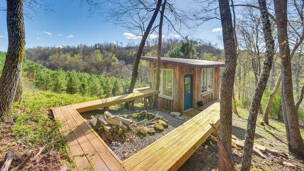 Eine Holzhütte mit einer Holzterrasse, umgeben von Bäumen und einer bewaldeten Landschaft.