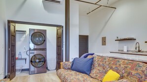 Una sala moderna con un sofá estampado, una lavadora y una cocina con encimera de mármol.