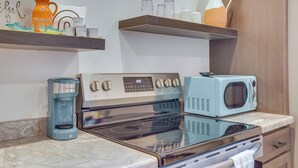 Una cocina con estufa, microondas, cafetera y estantes con utensilios de cocina.