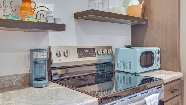 Una cocina con estufa, microondas, cafetera y estantes con utensilios de cocina.