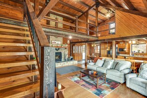 Un intérieur spacieux de chalet en bois, avec une cheminée, des poutres apparentes, un coin repas et un salon confortable doté d’un canapé et de fauteuils.