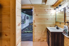 Un intérieur en bois, avec un mur en bois, un évier, un miroir et une porte donnant sur une autre pièce.