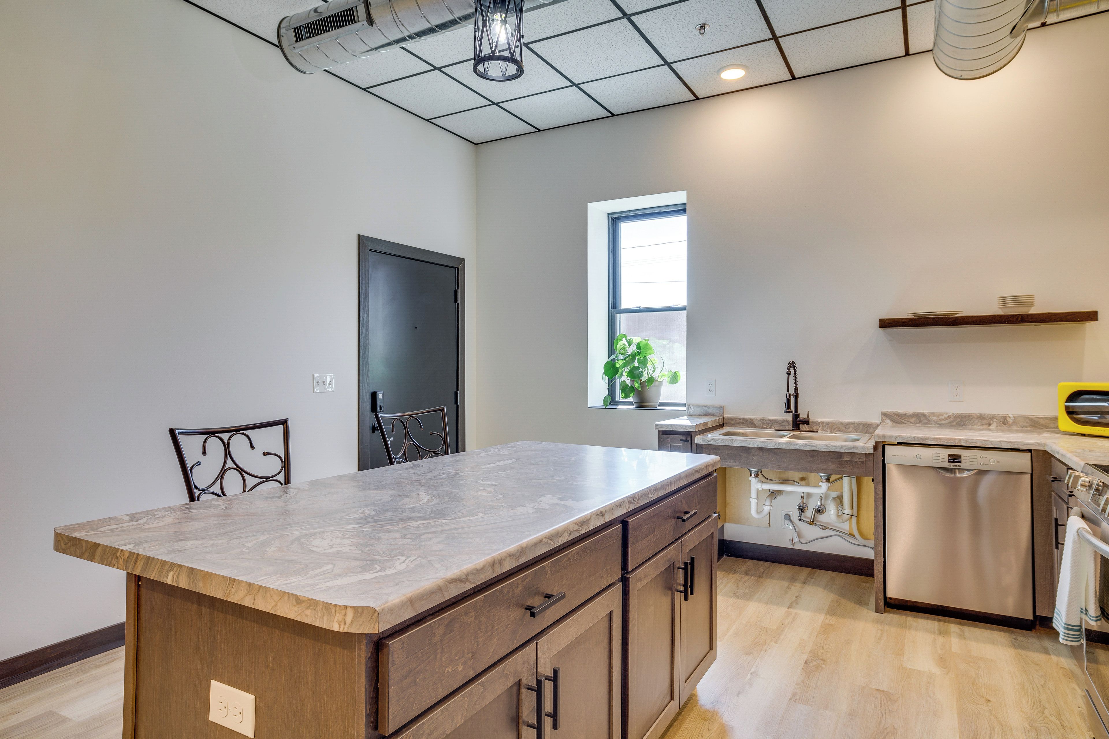 A kitchen with a marble countertop, wooden cabinets, a dishwasher, and a window with a plant.