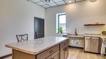 A kitchen with a marble countertop, wooden cabinets, a dishwasher, and a window with a plant.