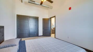 A bedroom with a bed, two doors, a ceiling fan, and an air conditioning unit.