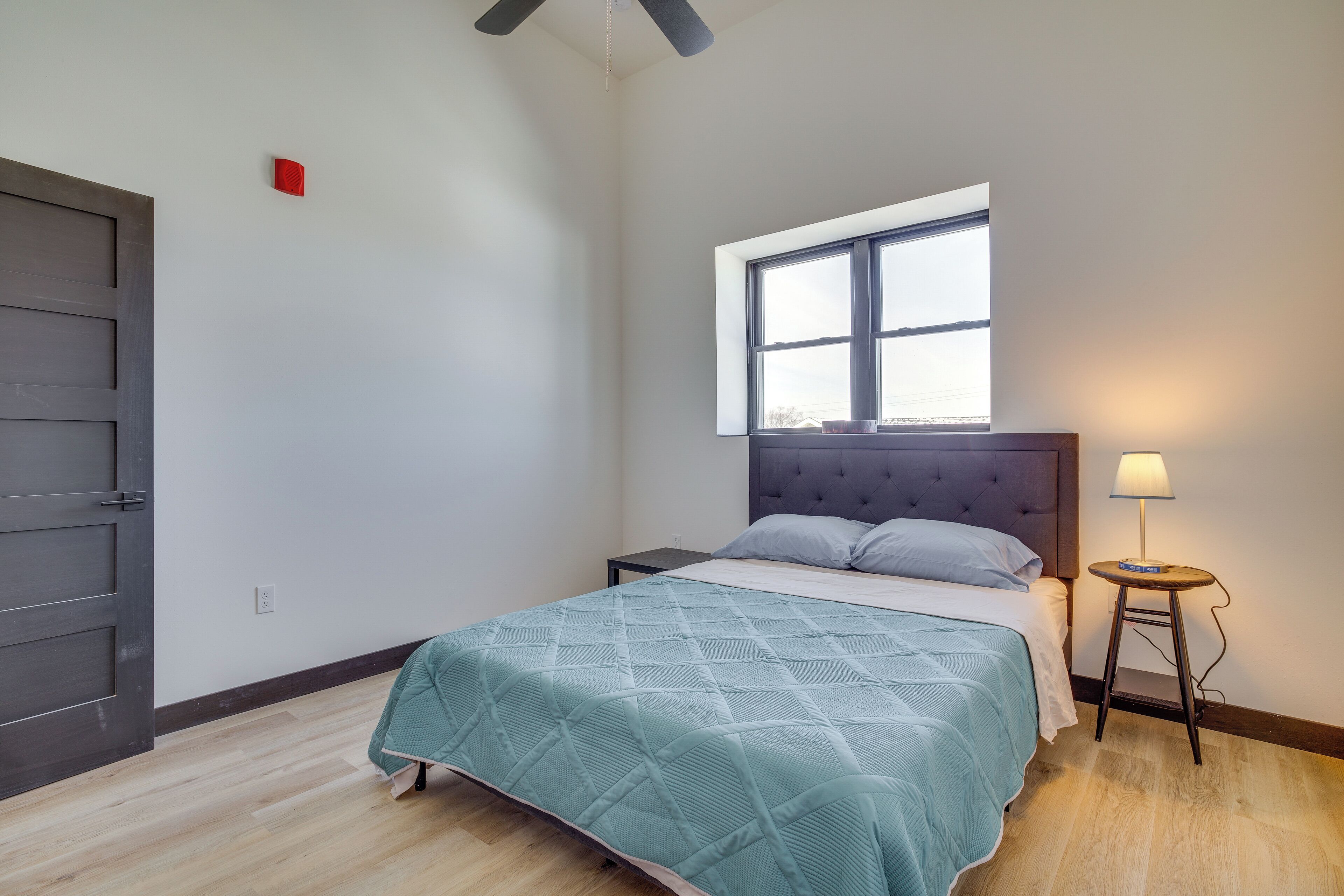 A bedroom with a bed, a window, a nightstand, and a lamp.