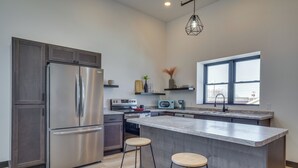 A modern kitchen with a stainless steel refrigerator, a built-in oven, and a large island with stools. - Modern, Open-concept Apartment: Downtown Cashton! (Cashton)