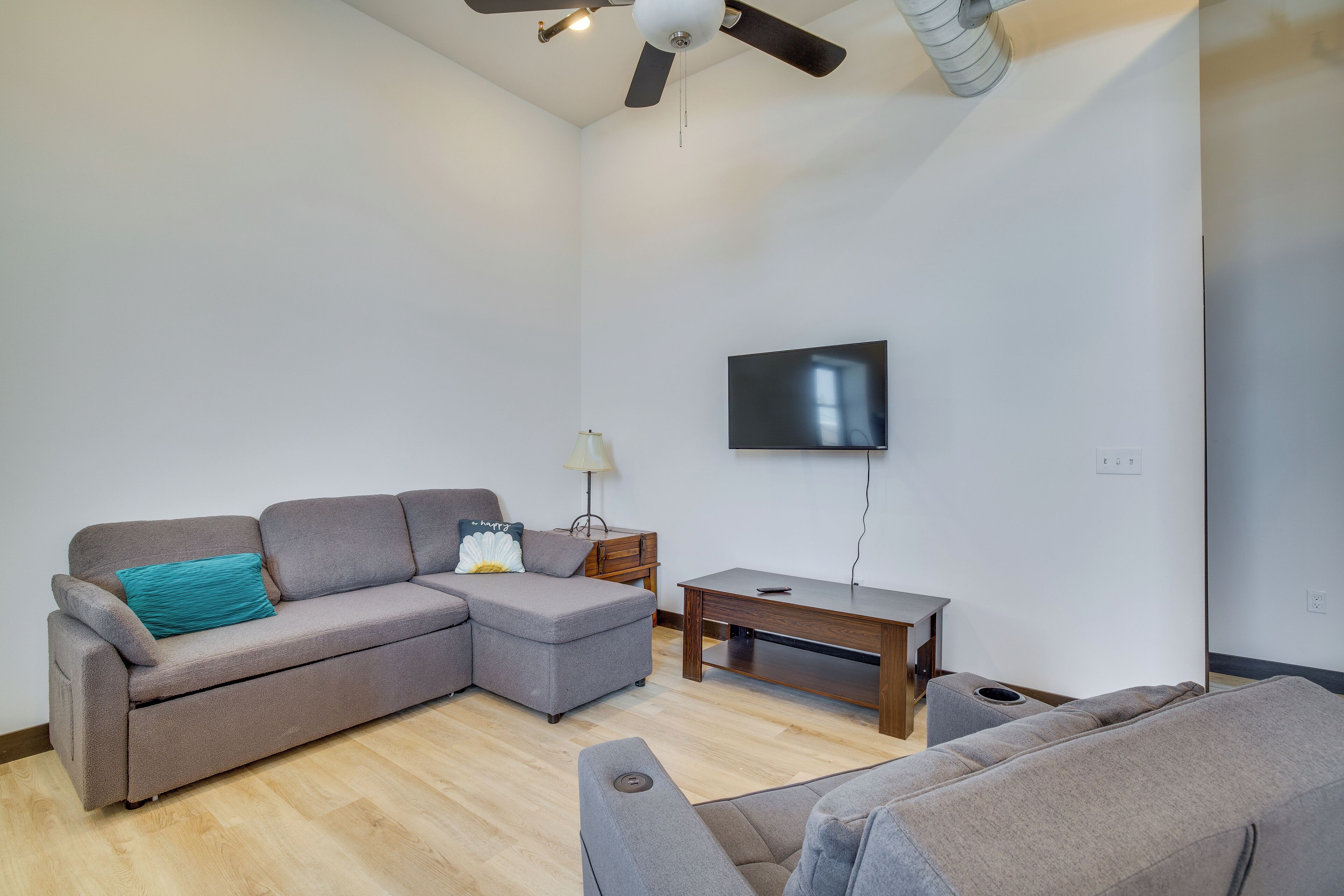 Una sala de estar moderna con un sofá seccional gris, una mesa de centro de madera y un televisor de pantalla plana montado en la pared.