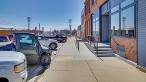 A parking lot with several vehicles, a sidewalk, and a building with large windows and a brick facade. - Modern, Open-concept Apartment: Downtown Cashton! (Cashton)